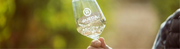 Copa de vino con el logo de Rueda en un viñedo