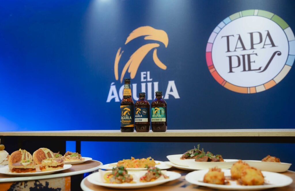 Botellas de cerveza El Águila en el festival Tapapiés con tapas variadas.