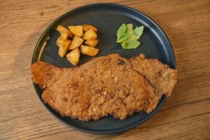 Milanesa acompañada de papas y hojas verdes en un plato negro