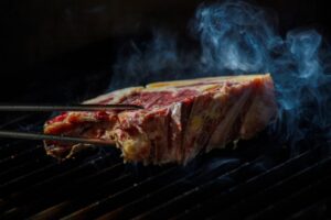Trozo de carne de vacuno asándose con humo en parrilla