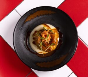 Plato de salchicha de cordero anticuchada con aligot y kimchi de chipotle.