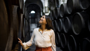 Mujer sonriendo en una bodega rodeada de barricas de vino