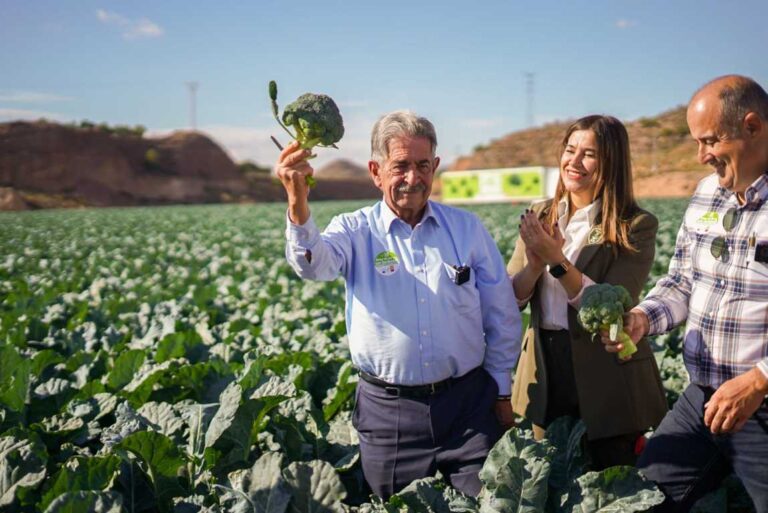 Miguel Ángel Revilla sostiene un brócoli en un campo con otros participantes.