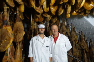 Dos hombres en una bodega de jamones colgados en Jabugo.