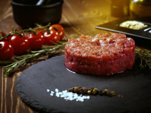 Steak tartar presentado en un plato negro con tomates y especias