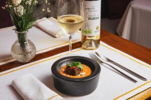 Plato gourmet acompañado de vino de la D.O. Rueda en un restaurante elegante.