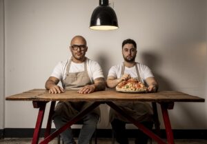 Dos chefs sentados en una mesa con una pizza en el centro