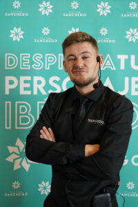 Hombre con auricular y camisa negra frente a fondo verde