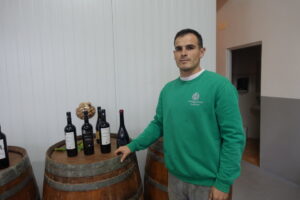 Hombre en bodega con botellas de vino artesanal en barricas de madera