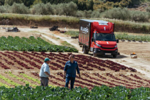 Dos hombres conversando en un campo con un camión de Eladio