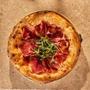 Pizza ibérica con jamón y rúcula sobre mesa de piedra