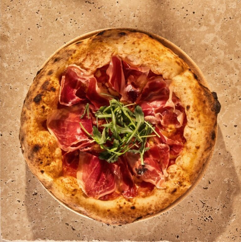 Pizza ibérica con jamón y rúcula sobre mesa de piedra