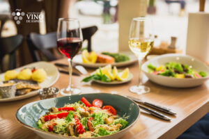 Plato de ensalada con vino tinto y blanco en mesa