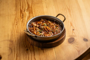 Plato de callos en una olla sobre una mesa de madera