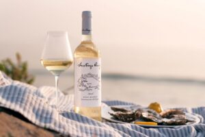 Botella de vino Santiago Ruiz junto a una copa y ostras en la playa