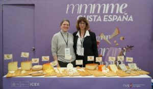 Mujeres en evento promocional con quesos españoles y cartel de Cheestories
