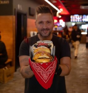 Hombre sosteniendo hamburguesas de La Vaquilla con bandana roja
