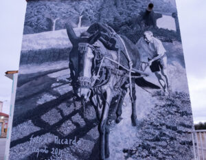 Mural de arte urbano que representa un hombre con un burro en el campo.