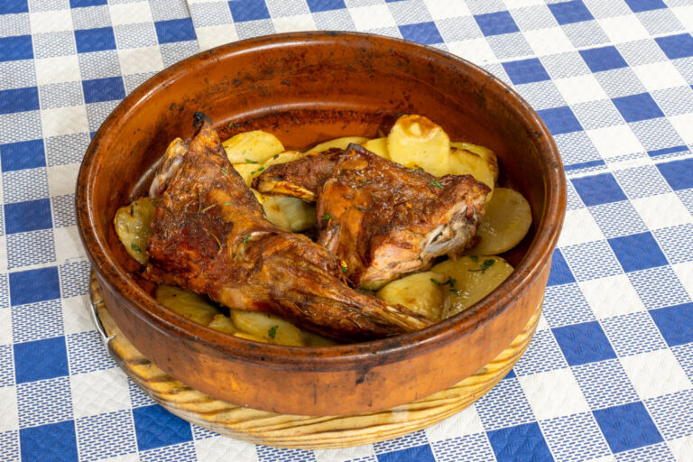 Plato de ternasco asado tradicional con patatas panadera en un recipiente de barro