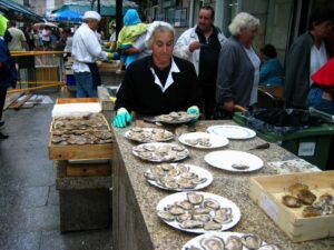 Hombre preparando ostras en un mercado gastronómico al aire libre.