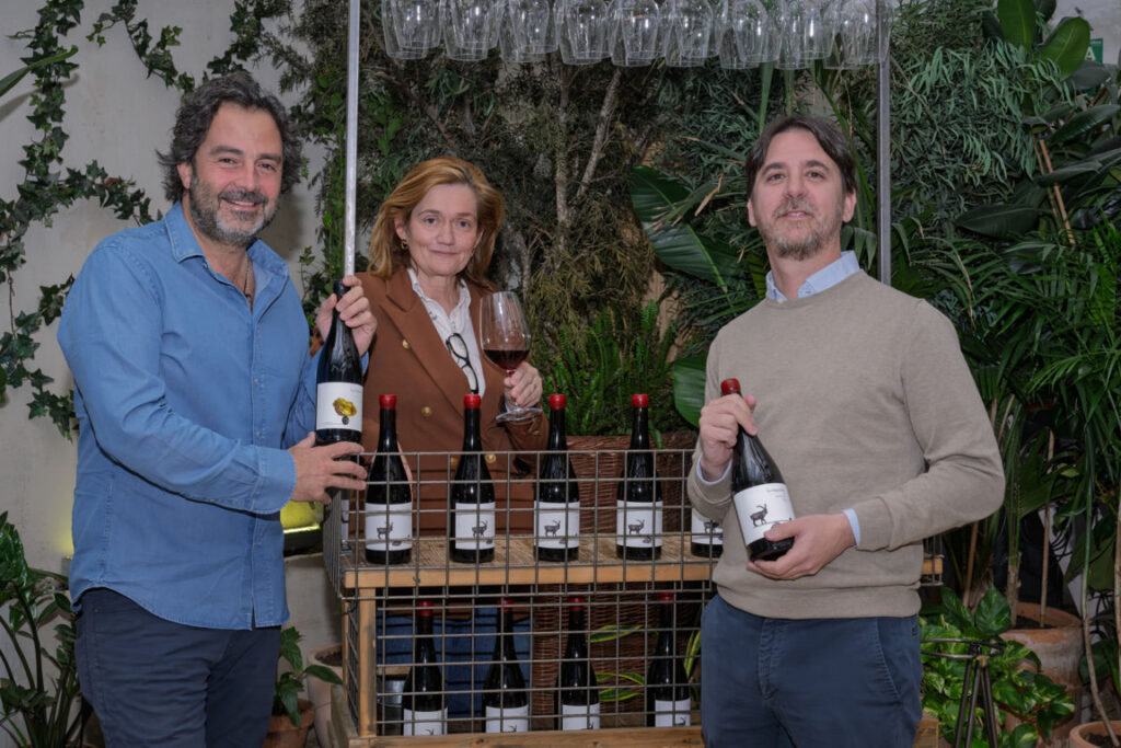 Tres personas sosteniendo botellas de vino en un evento de presentación