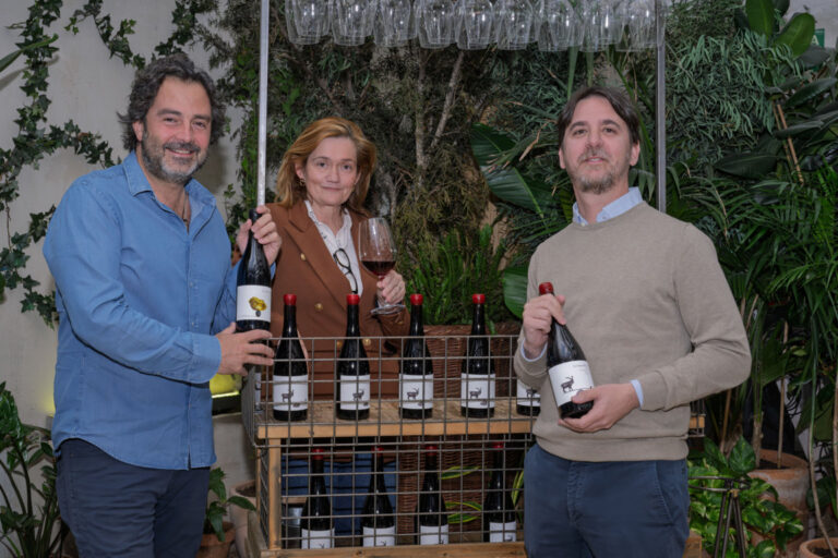 Tres personas sosteniendo botellas de vino en un evento de presentación