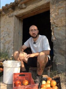 Hombre sentado en la entrada de una finca con tomates frescos.