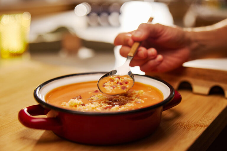 Persona sirviendo sopa con huevo en un plato rojo