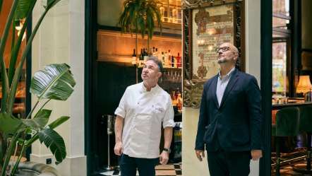 Dos hombres en un restaurante observando el entorno con plantas decorativas.