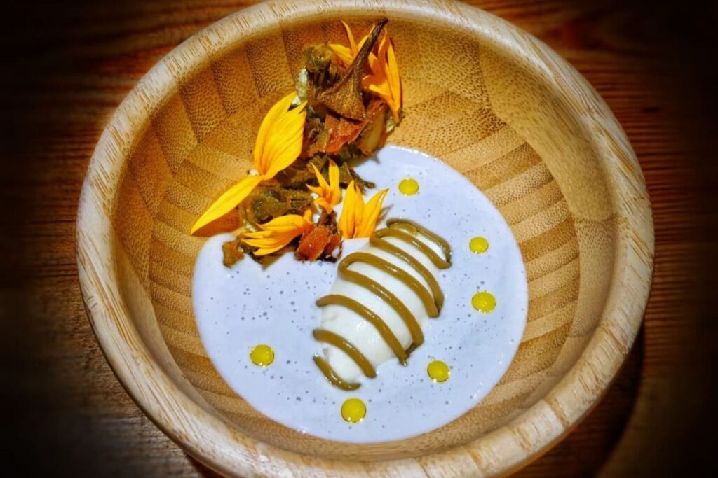 Plato de alcachofa girasol con flores y crema en un bol de madera