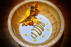 Plato de alcachofa girasol con flores y crema en un bol de madera