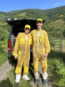 Dos apicultores en trajes amarillos sonríen en un paisaje montañoso.