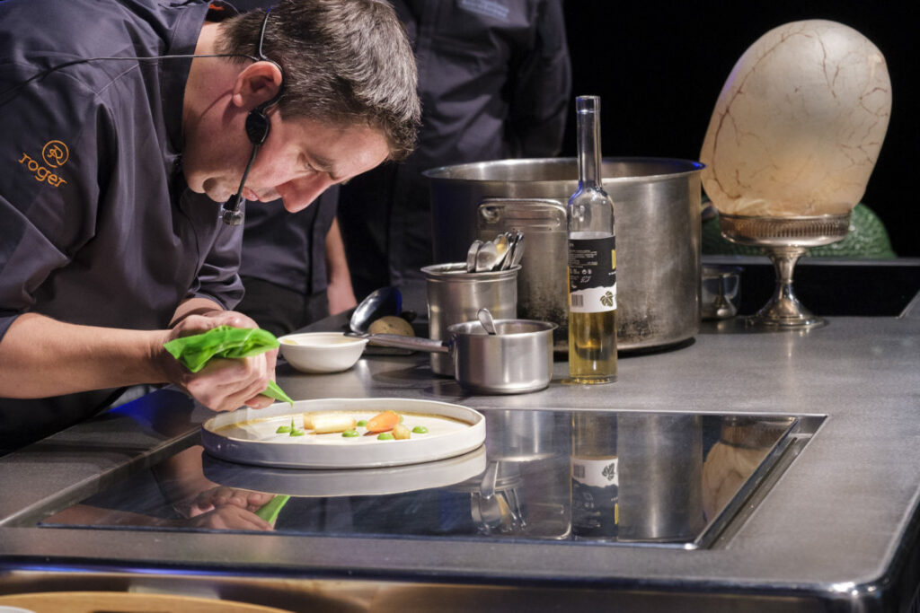 Chef preparando un plato con ingredientes frescos y vino en una cocina profesional.