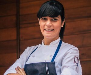 Chef Manu Buffara sonriendo con su uniforme de cocina en un ambiente acogedor