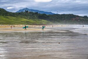 Surfistas caminando por la playa de Ribadesella con montañas al fondo