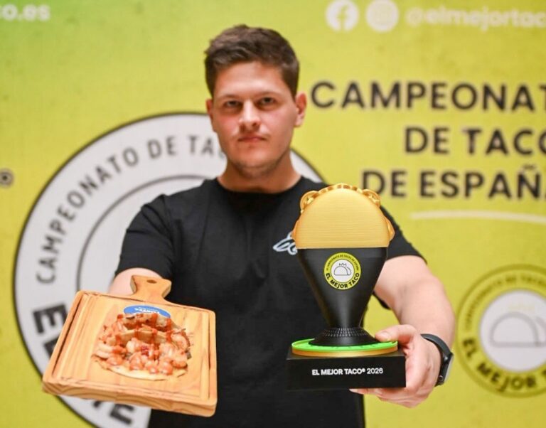 Un hombre sostiene un taco en una tabla y un trofeo del campeonato de tacos.
