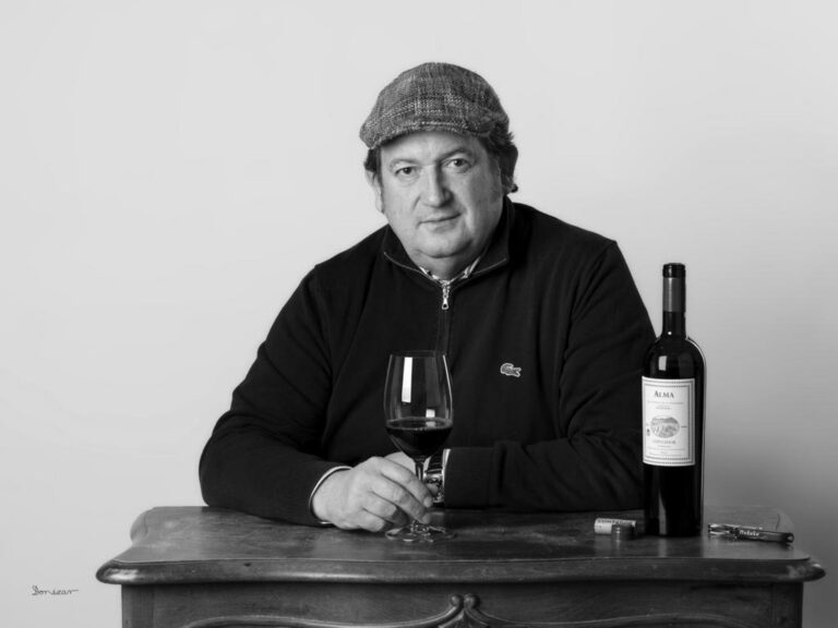 Benjamín Romeo sosteniendo una copa de vino junto a una botella de Alma.