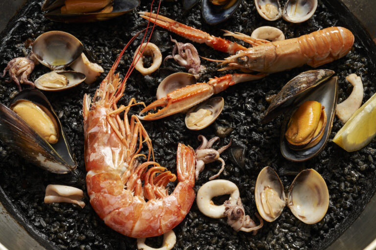 Paella negra con mariscos y langosta en un plato