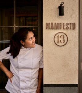 Chef Danitza Alpaca sonriendo junto al letrero de Manifesto 13