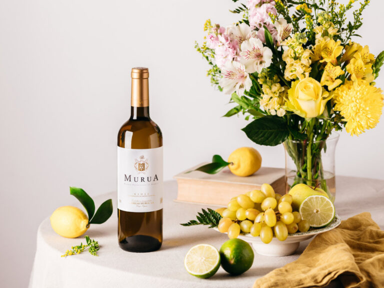 Botella de vino blanco Murua junto a frutas y flores