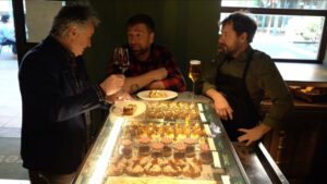 Tres hombres en un bar disfrutando de tapas y bebidas.