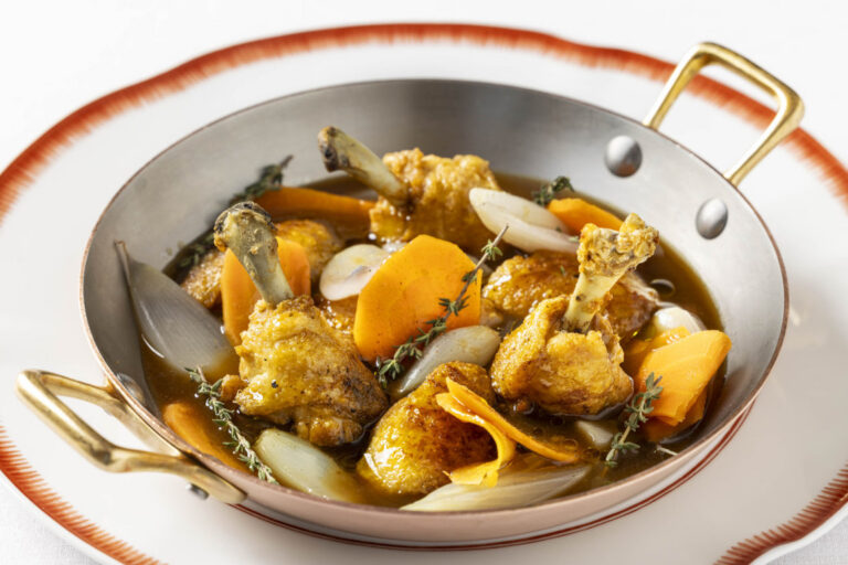 Alitas de pollo doradas con zanahoria y chalota en una cazuela metálica