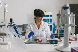 Una mujer con bata manipula trozos de alimento con una pipeta en un laboratorio.