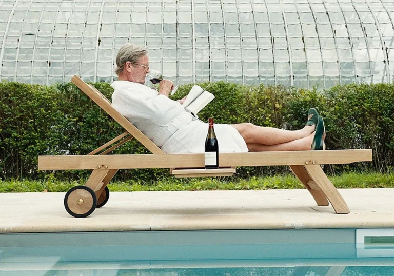 Hombre leyendo junto a una piscina con una copa de vino