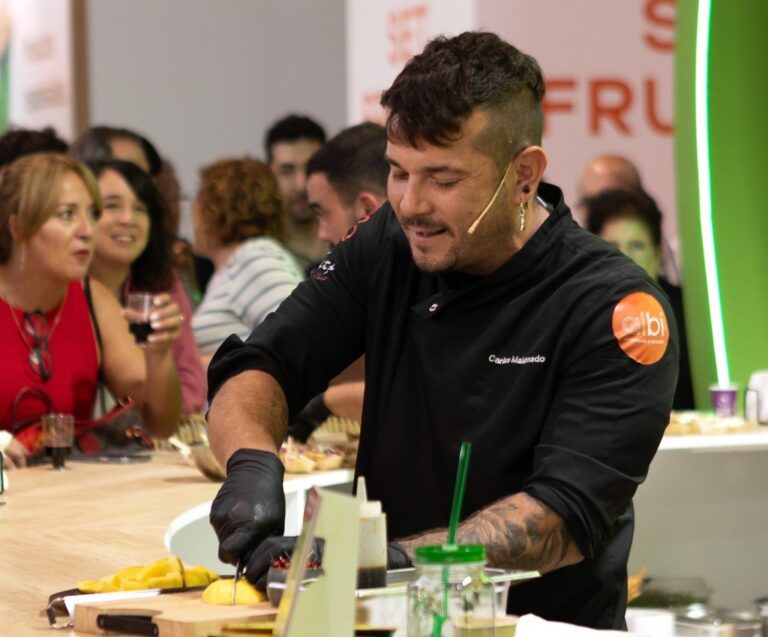 Carlos Maldonado, con chaqueta negra, prepara mango en una mesa ante varias personas.