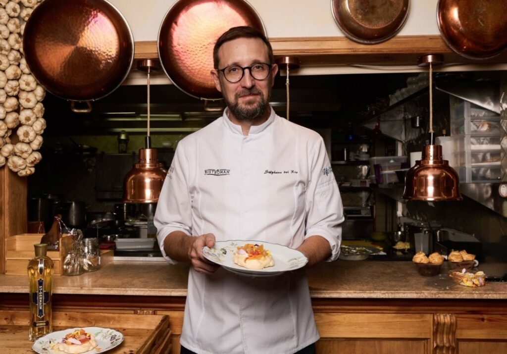 Hombre con chaqueta blanca sostiene un plato en una cocina de restaurante