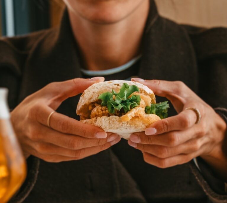 Persona sostiene con ambas manos un pequeño bocadillo con hojas verdes y relleno dorado