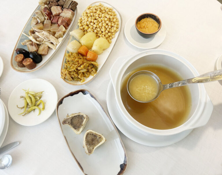 Cocido servido en fuentes con garbanzos, verduras, carnes, caldo y huesos de tuétano.