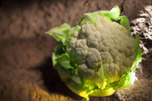 Coliflor blanca con hojas verdes creciendo en tierra bajo la luz del sol.