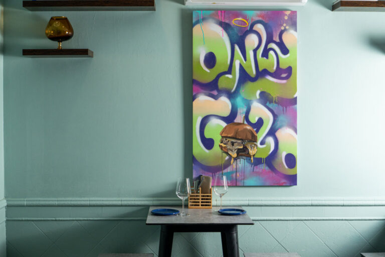 Rincón de comedor con mesa preparada y cuadro colorido de una hamburguesa.